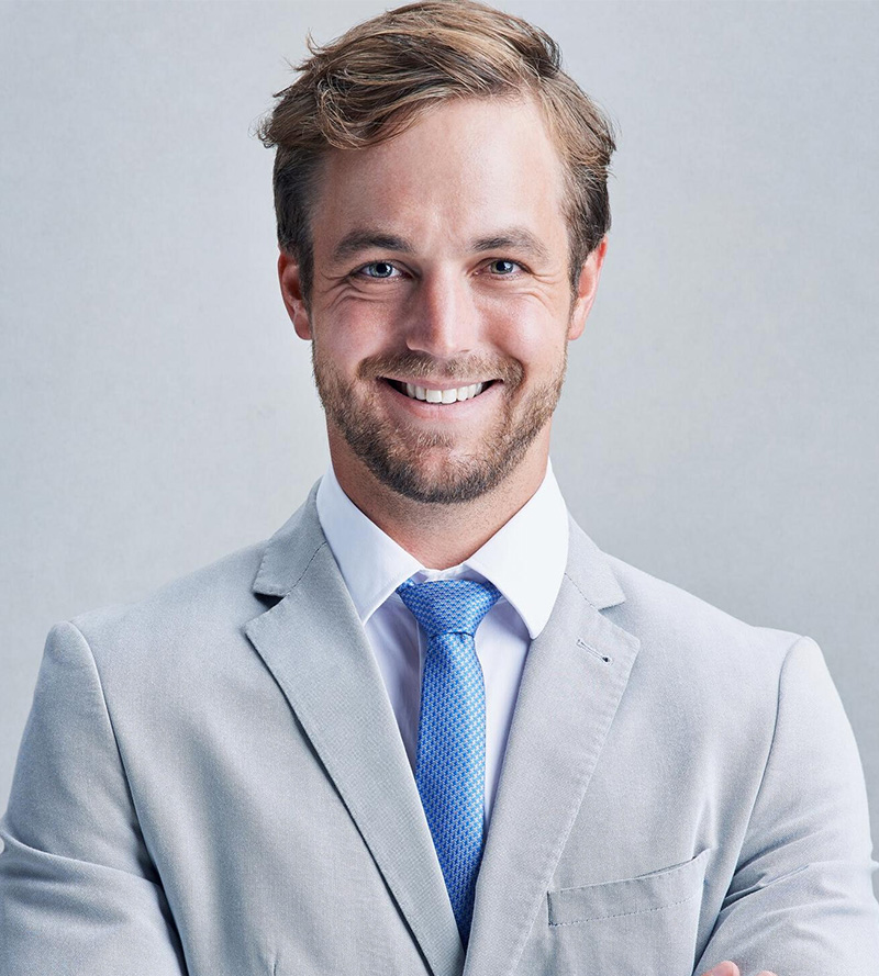 A smiling man in a gray suit and blue tie against a light gray background.