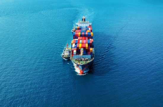 Aerial view of a large cargo ship filled with colorful containers sailing in a blue ocean.