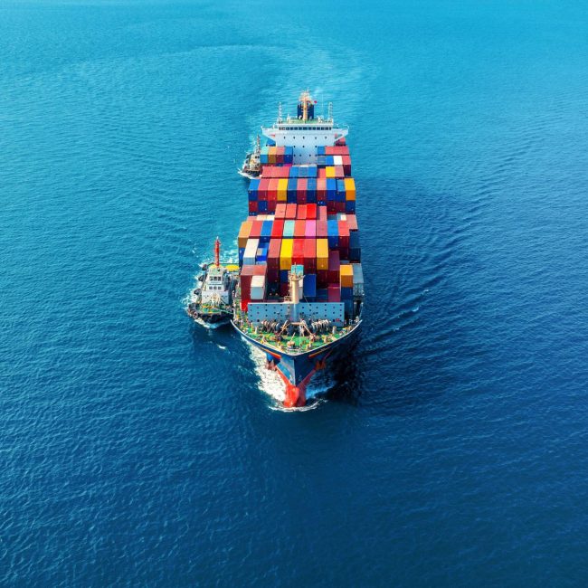 Aerial view of a large cargo ship filled with colorful containers sailing in a blue ocean.