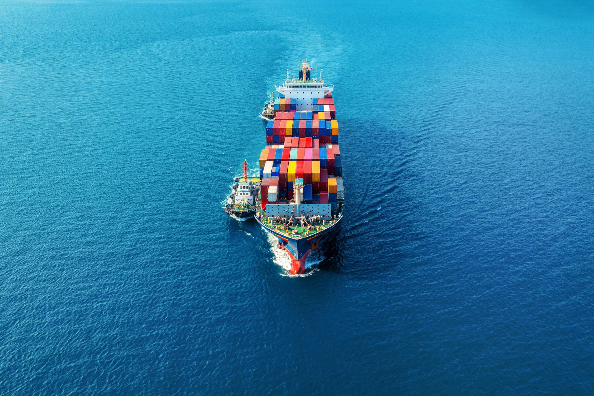 Aerial view of a large cargo ship filled with colorful containers sailing in a blue ocean.
