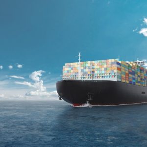 A large cargo ship laden with colorful containers sailing across a calm blue ocean under a clear sky.