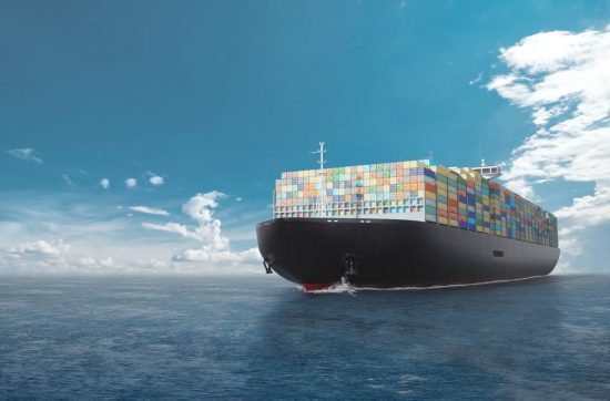 A large cargo ship laden with colorful containers sailing across a calm blue ocean under a clear sky.