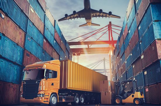 A cargo truck and forklift operate between stacked shipping containers at a port, as a plane descends overhead under a vibrant sunset sky.
