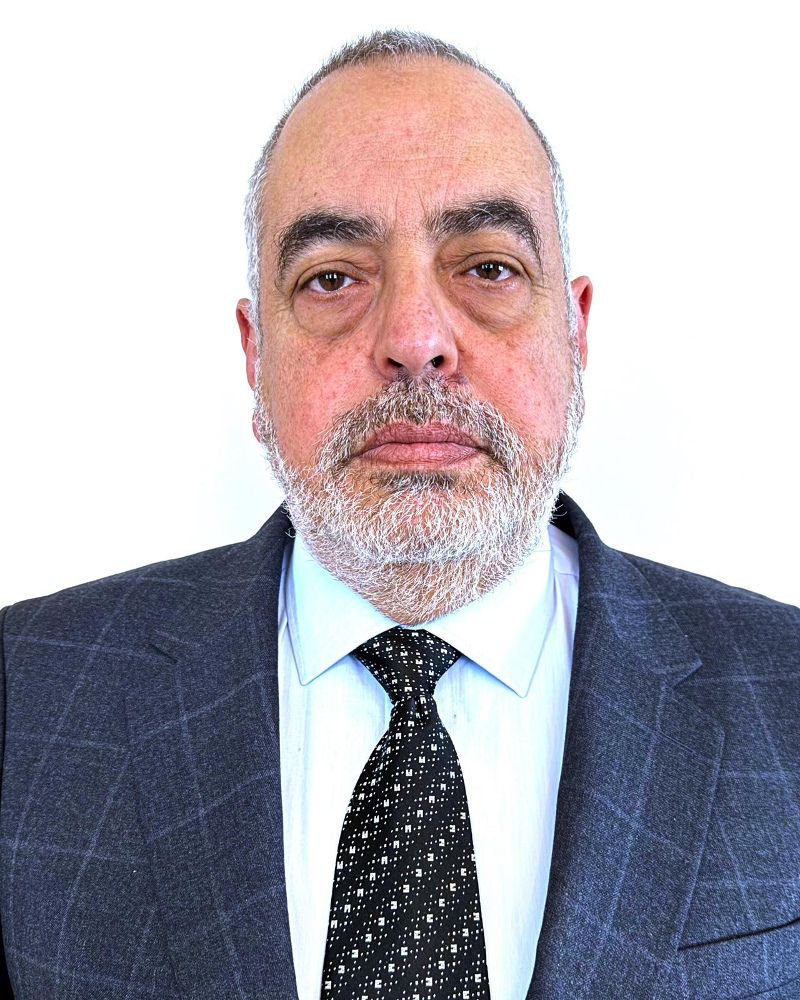 Portrait of a middle-aged man with a beard, wearing a suit and tie, against a white background.